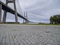 a long bridge that has a big brick walkway going under it to a field with trees in the background