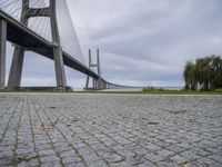 a long bridge that has a big brick walkway going under it to a field with trees in the background