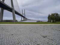 a long bridge that has a big brick walkway going under it to a field with trees in the background