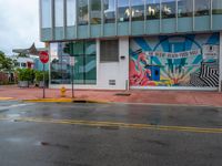 the wall on the building is covered with large murals and a yellow stop sign on a wet road