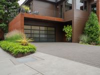 the driveway has a walkway and landscaping along it and is a brown building with three stories