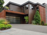 the driveway has a walkway and landscaping along it and is a brown building with three stories