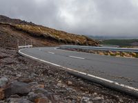 the car is driving on the road in front of mountains and rocks under a cloudy sky