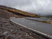 the car is driving on the road in front of mountains and rocks under a cloudy sky