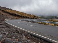 the car is driving on the road in front of mountains and rocks under a cloudy sky