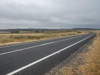 an empty highway on a cloudy day with grass and weeds along the side of the road