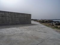 an empty concrete beach with a wall in the background on top of it next to water