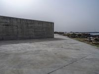 an empty concrete beach with a wall in the background on top of it next to water