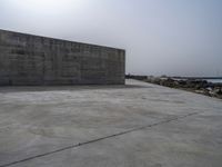 an empty concrete beach with a wall in the background on top of it next to water