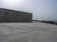 an empty concrete beach with a wall in the background on top of it next to water