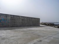 an empty concrete beach with a wall in the background on top of it next to water