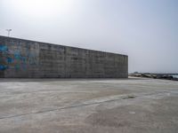 an empty concrete beach with a wall in the background on top of it next to water