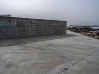 an empty concrete beach with a wall in the background on top of it next to water