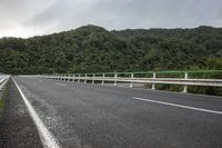 an empty road on a cloudy day in the countryside near trees and hills behind the bridge