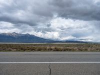 a red stop sign on an empty street next to a mountain range on a cloudy day