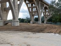 the view from underneath of a bridge on a partly cloudy day, including piles of dirt and sand