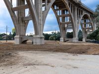 the view from underneath of a bridge on a partly cloudy day, including piles of dirt and sand