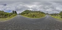 a wide open road stretches out into the sky near grassy hills and trees on both sides