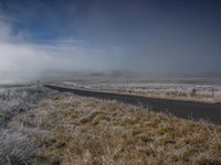 the road winds through the field on a winter morning with steam in the air and clouds