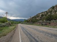 a road with telephone poles on the side of it and mountains in the distance under a cloudy sky