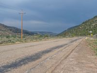 the empty roadway is lined with utility poles and telephone lines and mountains behind it, some plants