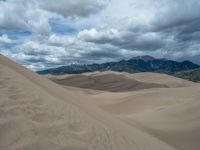 sand dune dunes in a desert area under a cloudy sky and mountains as seen from above