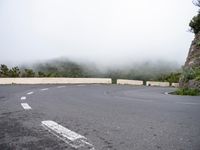 an empty, deserted road with curves and trees on the side of it in the mist