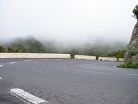 an empty, deserted road with curves and trees on the side of it in the mist