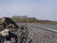 a motorcycle sits on the side of the road in front of the gravel road with trees