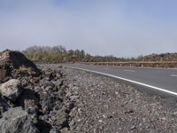 a motorcycle sits on the side of the road in front of the gravel road with trees