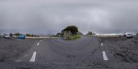 cars parked in a lot behind a stone wall with two ramps, in front of a hill that is just below the clouds