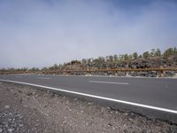 a empty roadway with a big pile of black rocks on it and a line of trees