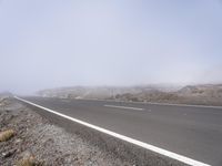 a road near the mountain side in the foggy sun day, and on the opposite bank are hills