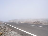 a road near the mountain side in the foggy sun day, and on the opposite bank are hills