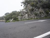 a lone bike is standing by a steep cliff face and road leading the hill,