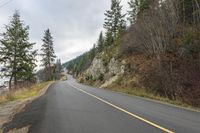 a man riding a motorcycle down a curvy road next to pine trees and mountains