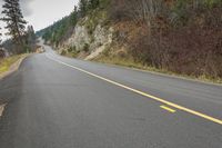 a man riding a motorcycle down a curvy road next to pine trees and mountains