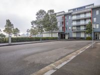 a empty, gray street in front of apartment buildings with trees, fencing and bushes