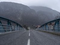 an empty street with mountains behind it and bridge in the middle of the road, with no traffic on it