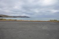 a large empty parking lot next to the water and hills overlooking the ocean as an area to stretch out