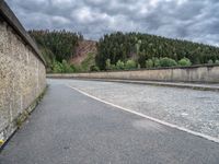 concrete walkway with trees and fenced in area on opposite sides of the road and one side of the road