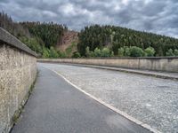 concrete walkway with trees and fenced in area on opposite sides of the road and one side of the road