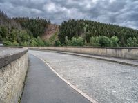 concrete walkway with trees and fenced in area on opposite sides of the road and one side of the road