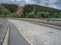 concrete walkway with trees and fenced in area on opposite sides of the road and one side of the road