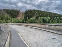 concrete walkway with trees and fenced in area on opposite sides of the road and one side of the road