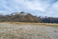 a bench in the middle of a gravel road overlooking mountains and snow covered peakss