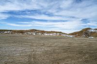 a large open field that is dirt and dirt is snow and blue skies above the mountain