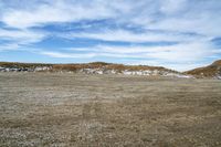 a large open field that is dirt and dirt is snow and blue skies above the mountain