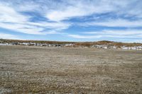 a large open field that is dirt and dirt is snow and blue skies above the mountain