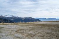 a sandy field with mountains on both sides, a few rocks and grass in the middle